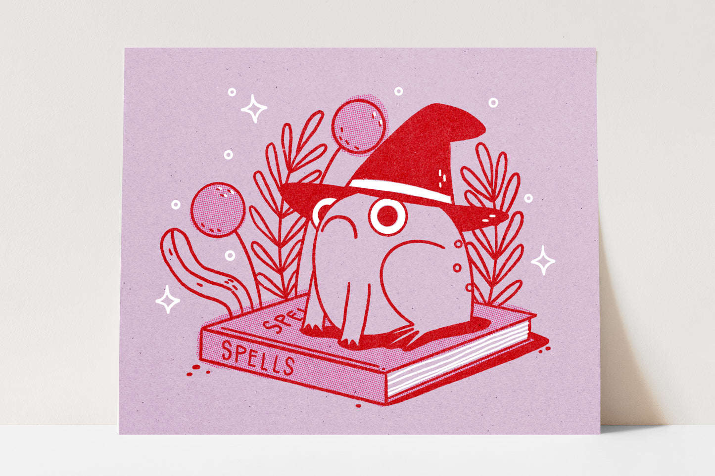 Print of an illustration of a frog sitting on a book of spells wearing a witch's hat.