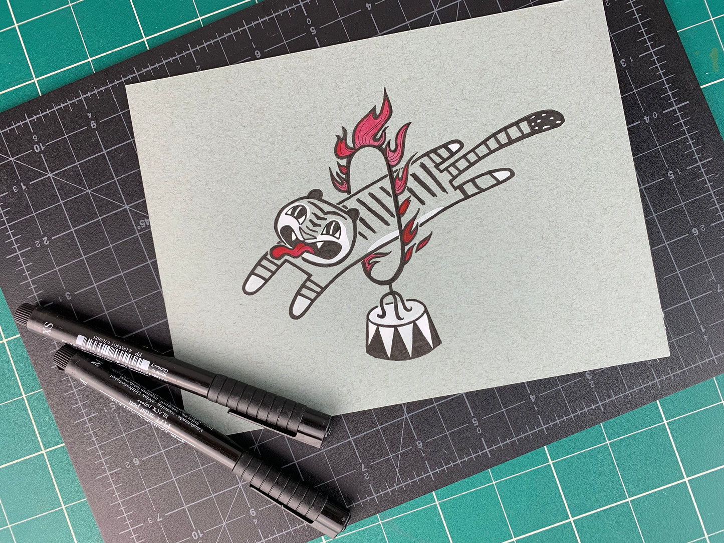 Studio shot of an original illustration of a tiger with a long tongue sticking out as they jump through a circus style ring of fire. Made using ink, watercolor, and gouache.