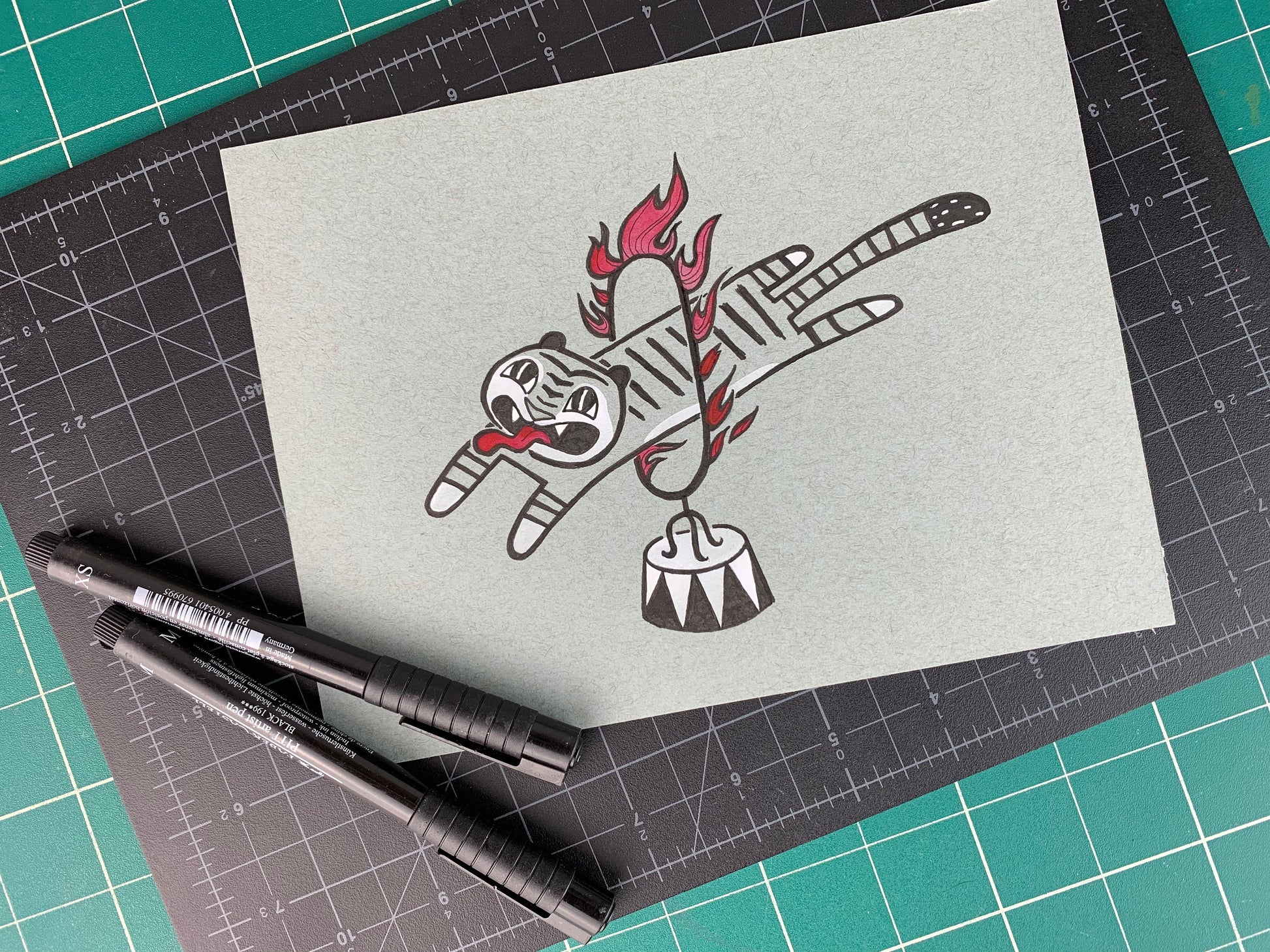 Studio shot of an original illustration of a tiger with a long tongue sticking out as they jump through a circus style ring of fire. Made using ink, watercolor, and gouache.