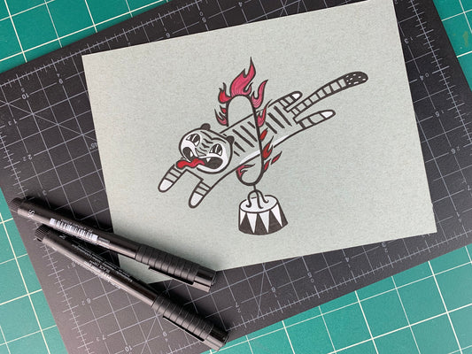 Studio shot of an original illustration of a tiger with a long tongue sticking out as they jump through a circus style ring of fire. Made using ink, watercolor, and gouache.