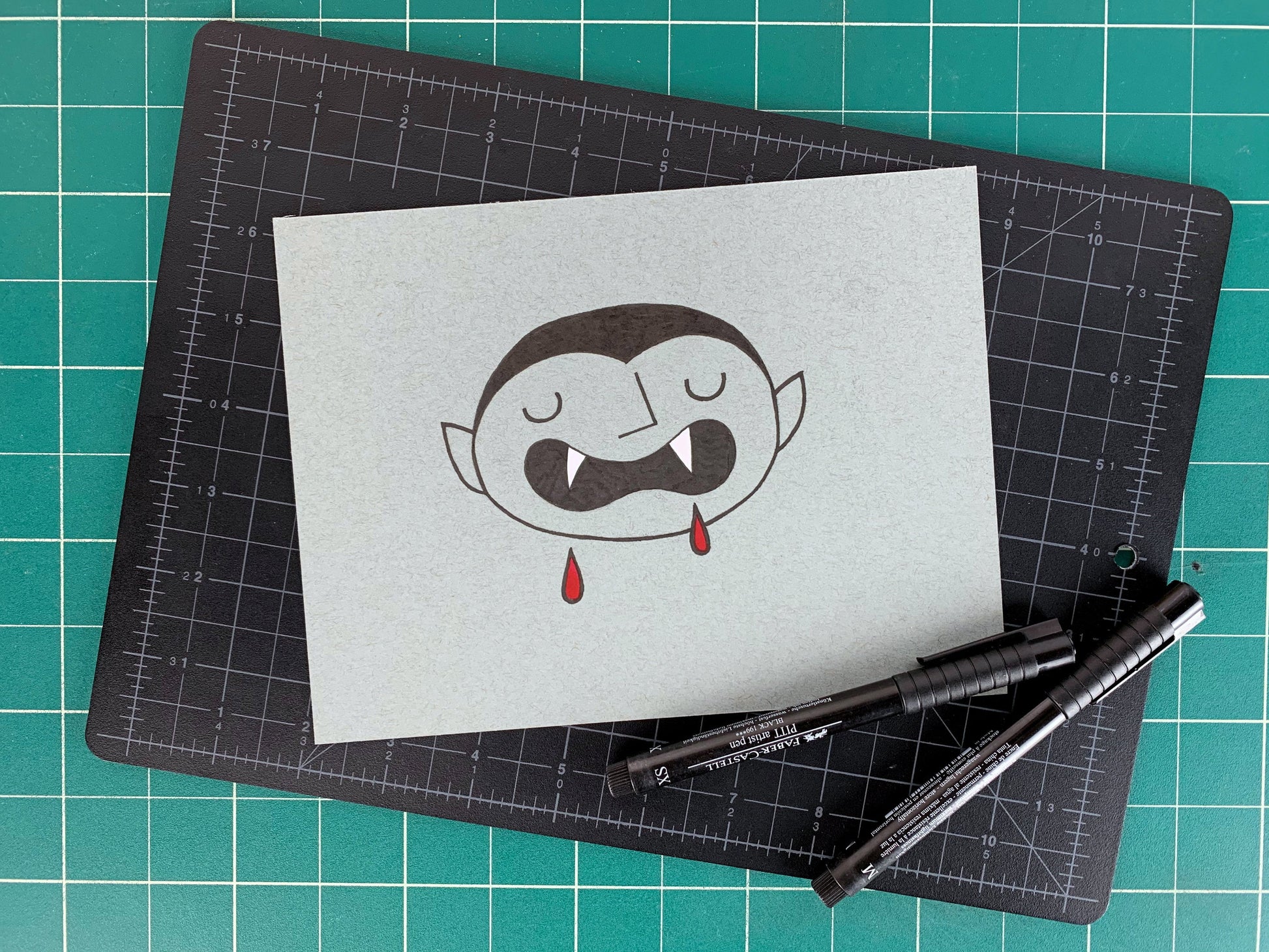 Studio shot of an original illustration of a cute vampire with big sharp teeth and blood drips. Made using ink, watercolor, and gouache.