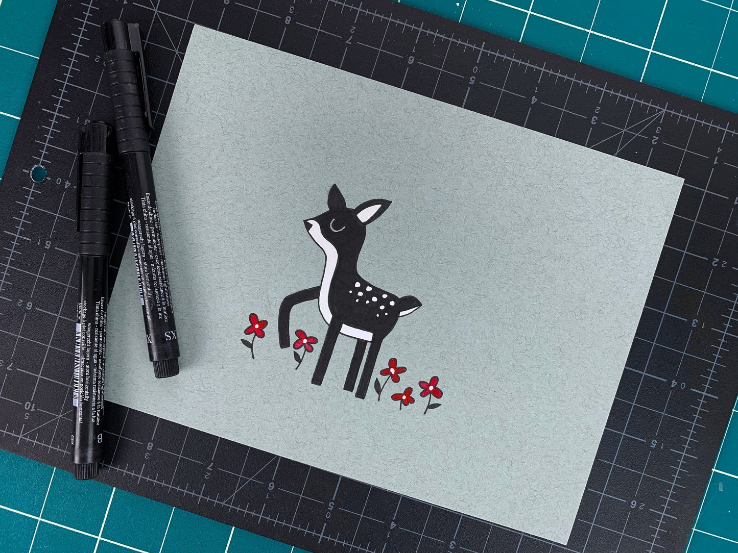 Studio shot of an original illustration of a little deer walking through a field of little flowers. Made using ink, watercolor, and gouache.