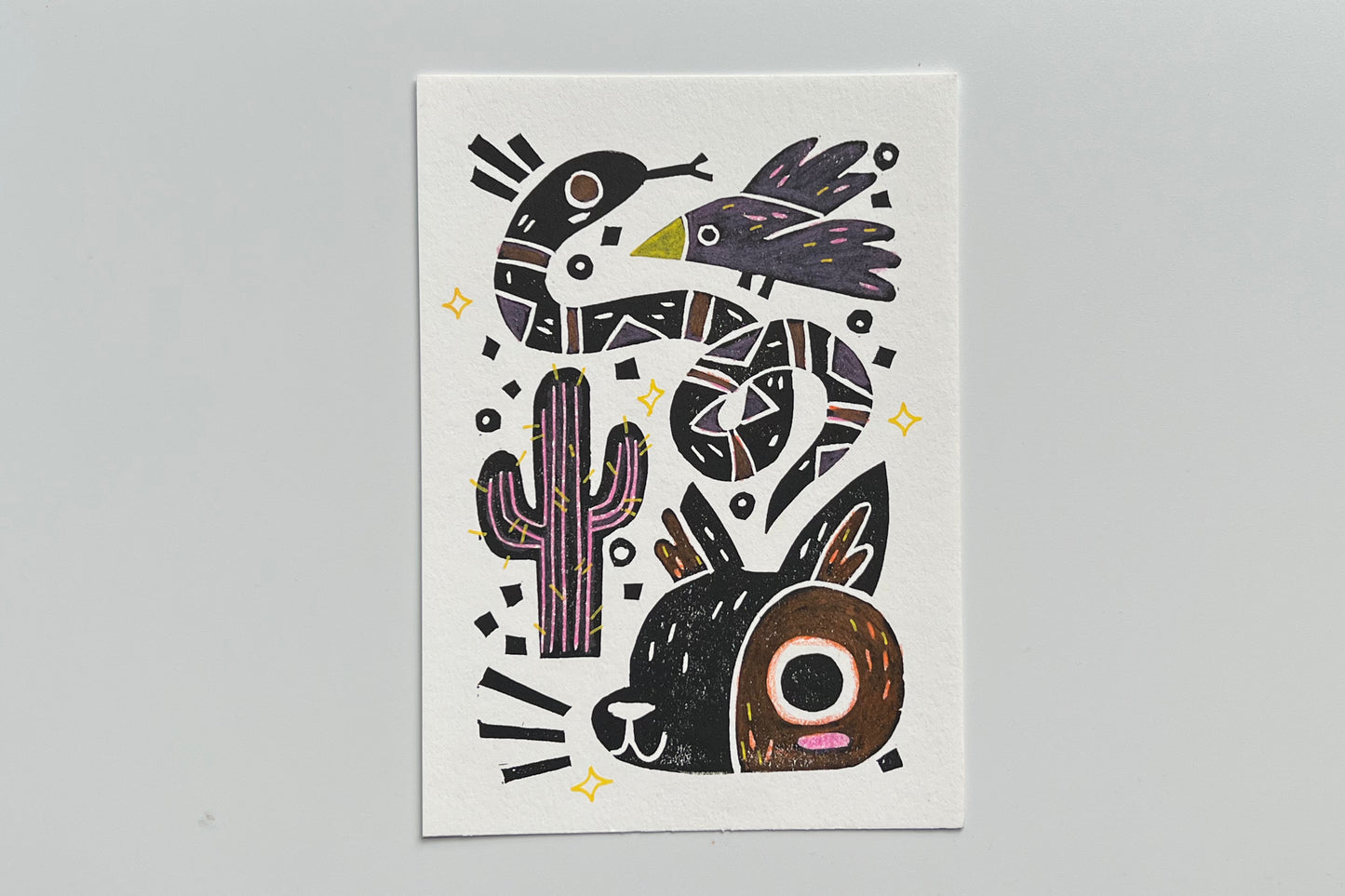 Black ink block print of a bird, snake, cactus, and coyote with colored pencil and POSCA pen coloring.