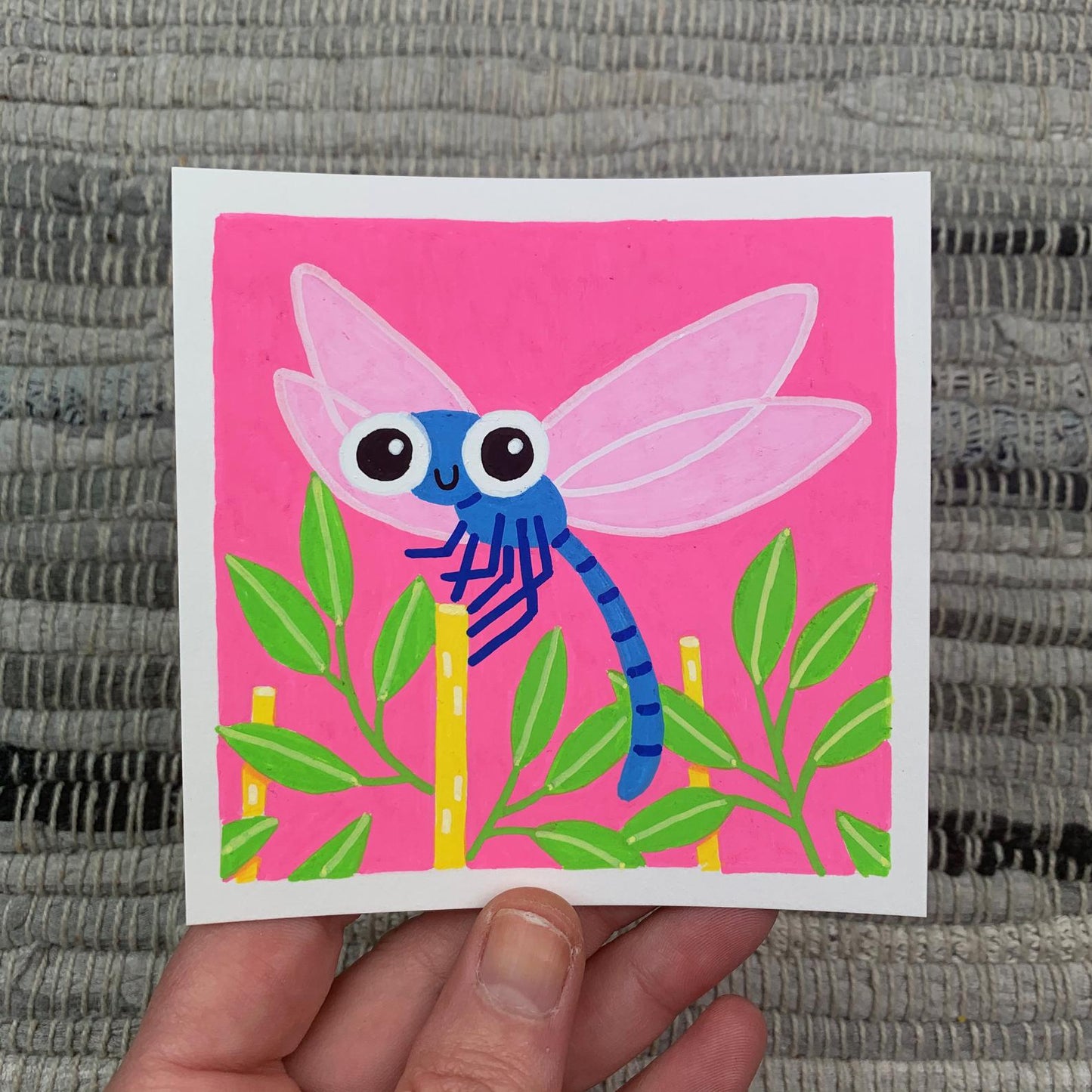 Original artwork of a cute dragonfly landing on a reed on a pink background. Materials used: Uni-Posca paint markers.