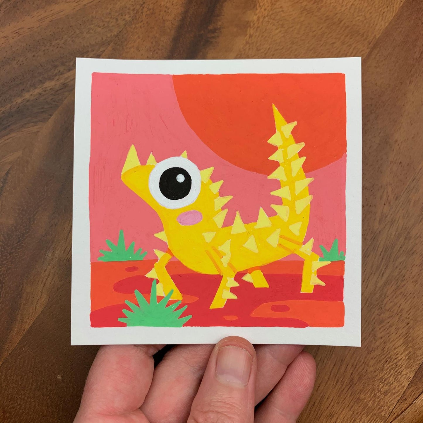 Original artwork of a cute yellow lizard covered in spikes on a red desert scene. Materials used: Uni-Posca paint markers.