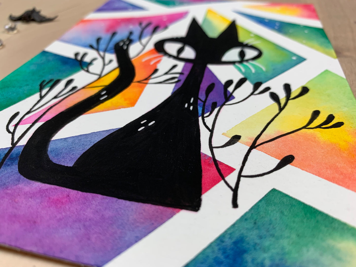 Original artwork depicting a colorful geometric watercolor and gouache painting of a black cat.