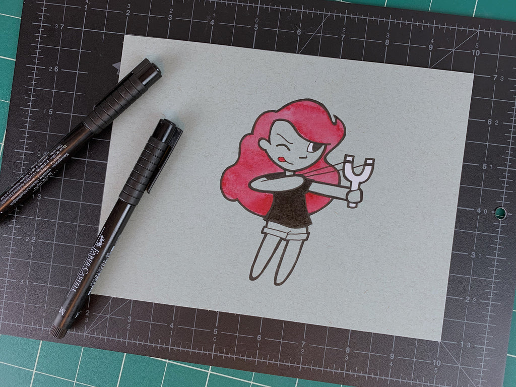 Studio shot of an original illustration of a red headed girl sticking her tongue out while she aims with her slingshot. Made using ink, watercolor, and gouache.