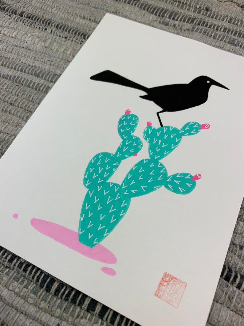Original artwork of a black bird, boat-tailed grackle, standing on a prickly pear cactus.