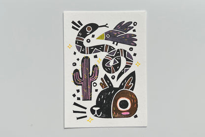 Black ink block print of a bird, snake, cactus, and coyote with colored pencil and POSCA pen coloring.
