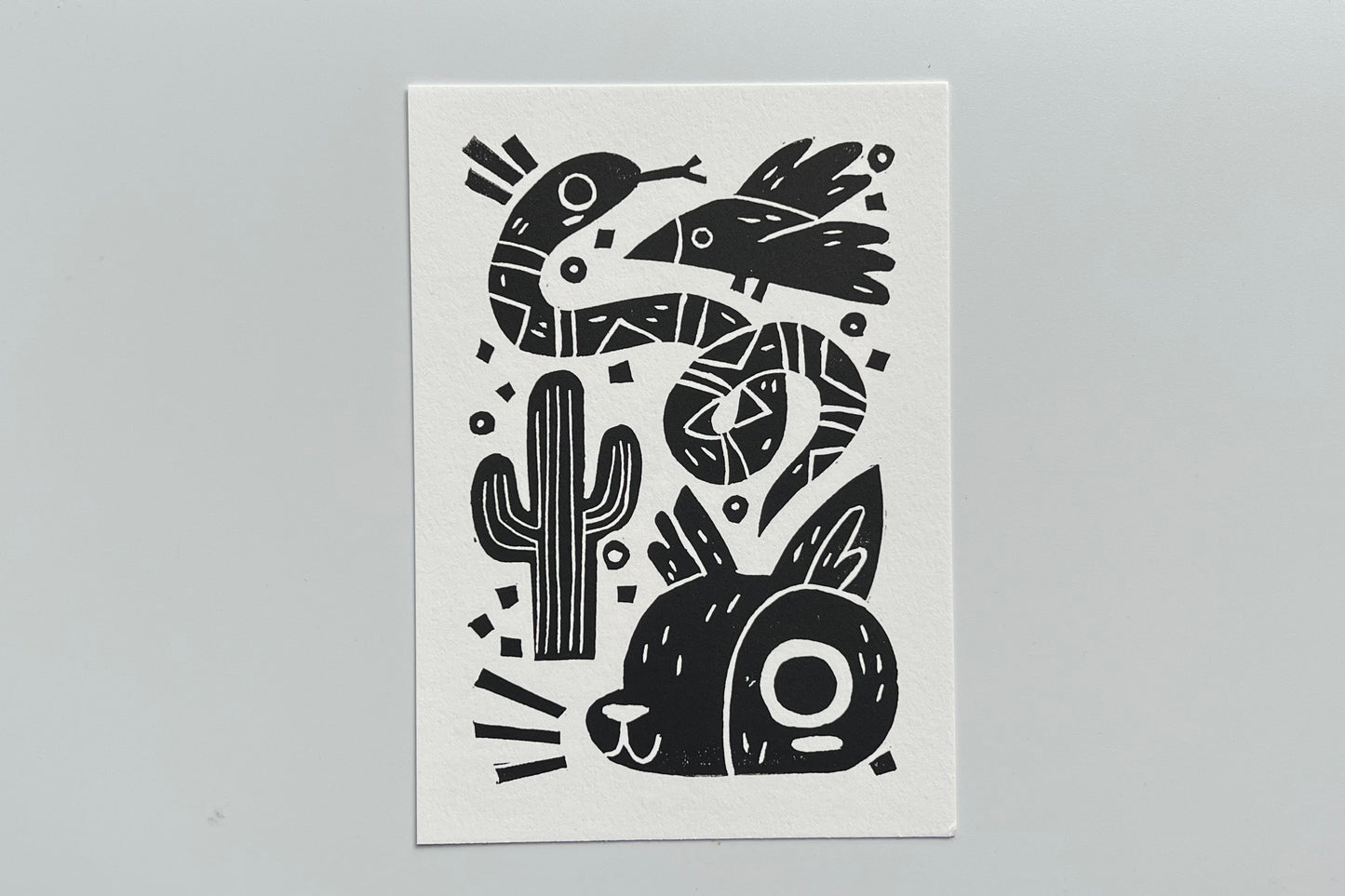 Black ink block print of a bird, snake, cactus, and coyote.