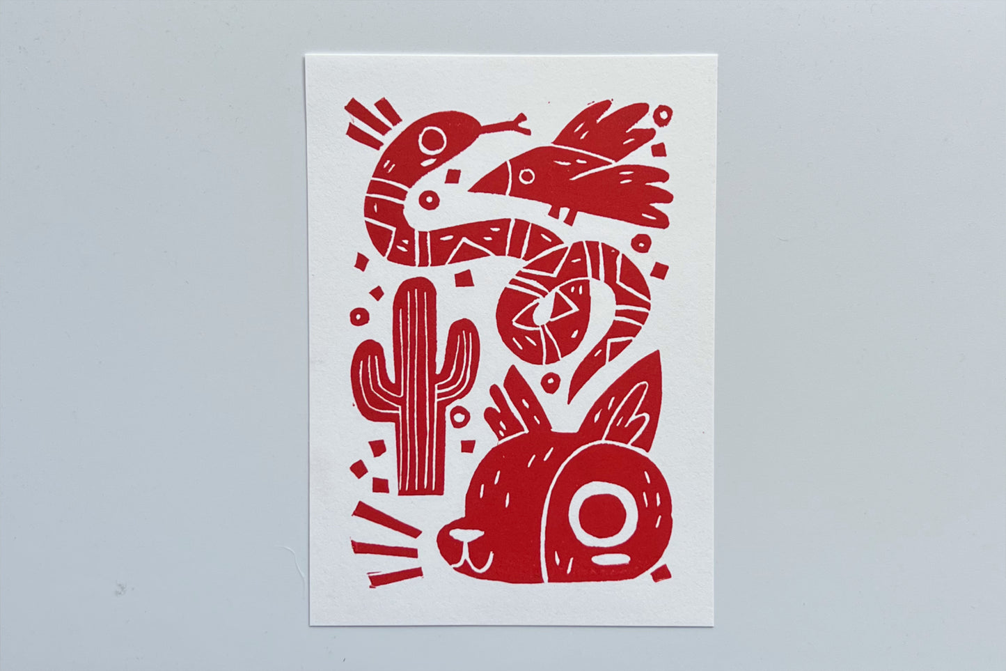 Red ink block print of a bird, snake, cactus, and coyote.