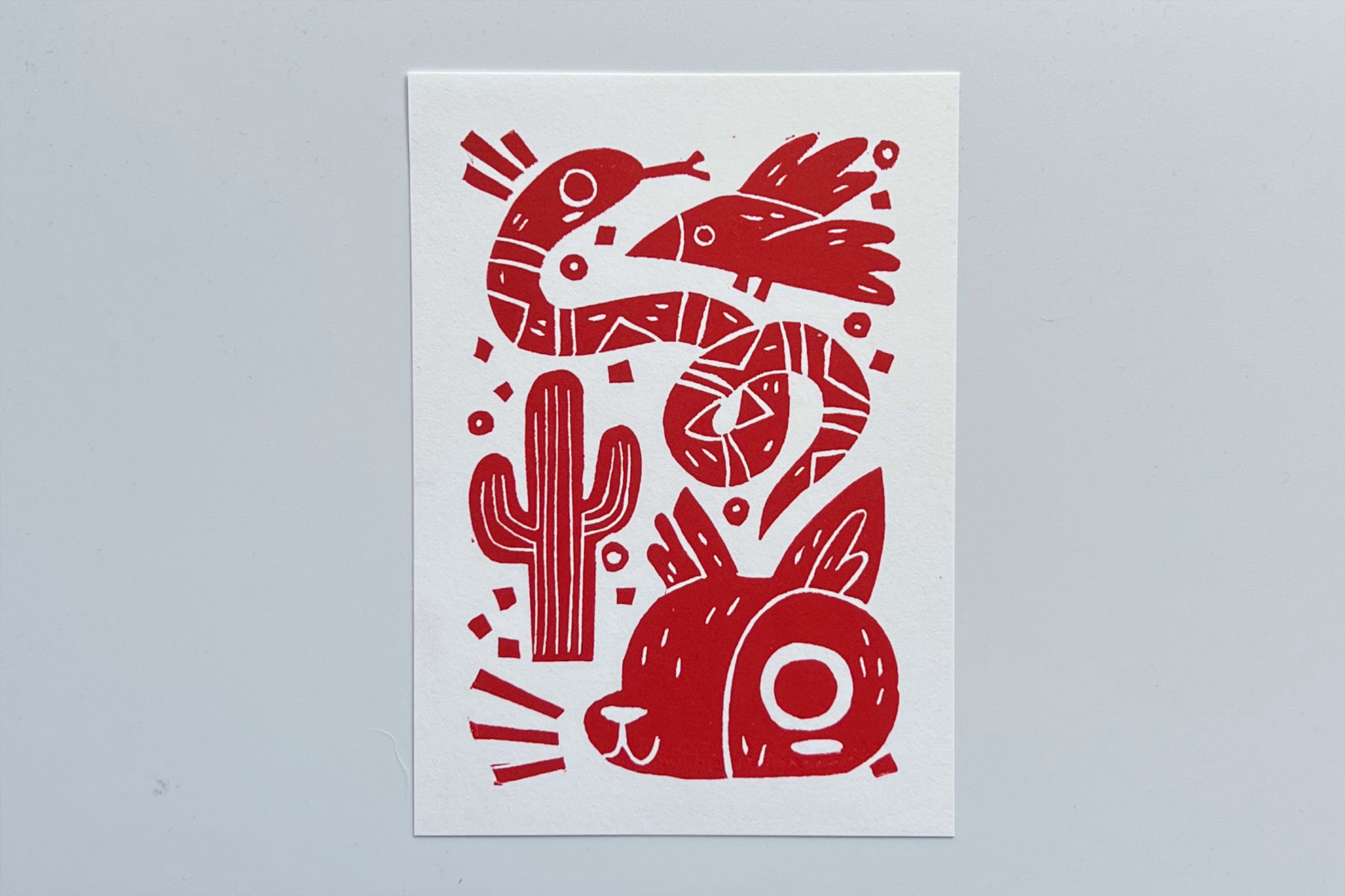 Red ink block print of a bird, snake, cactus, and coyote.