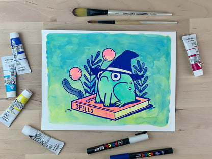 Painting of a frog with a witch's hat sitting on top of a book of spells with some flowers in the background.