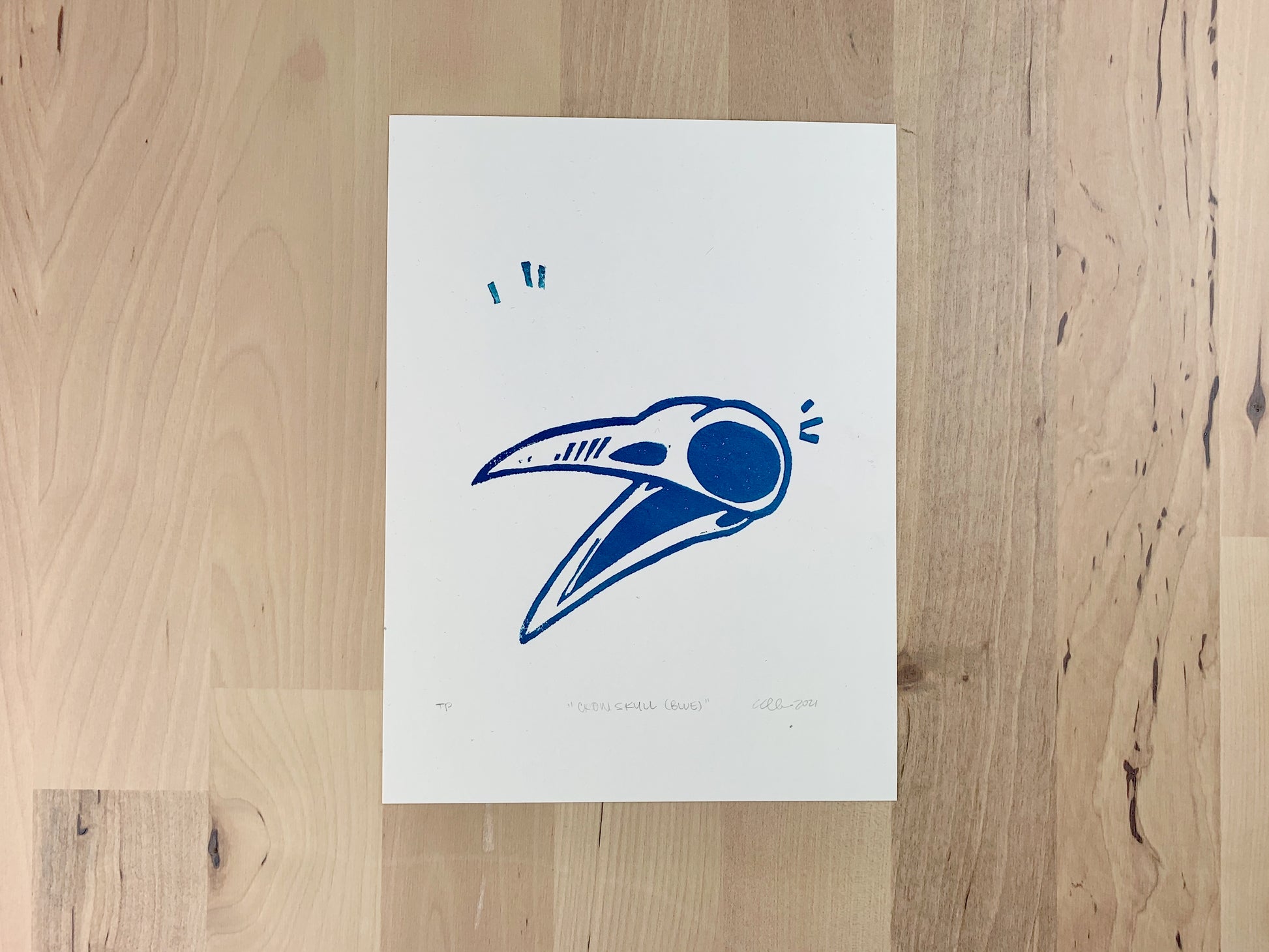 Original art test print by Amber Orenstein. Block print of a blue crow skull.