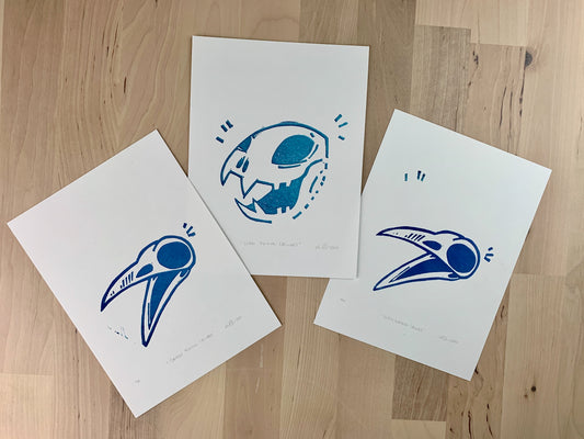 Original art test print by Amber Orenstein. Three block prints of a blue animal skulls, two crows and a big cat lion.