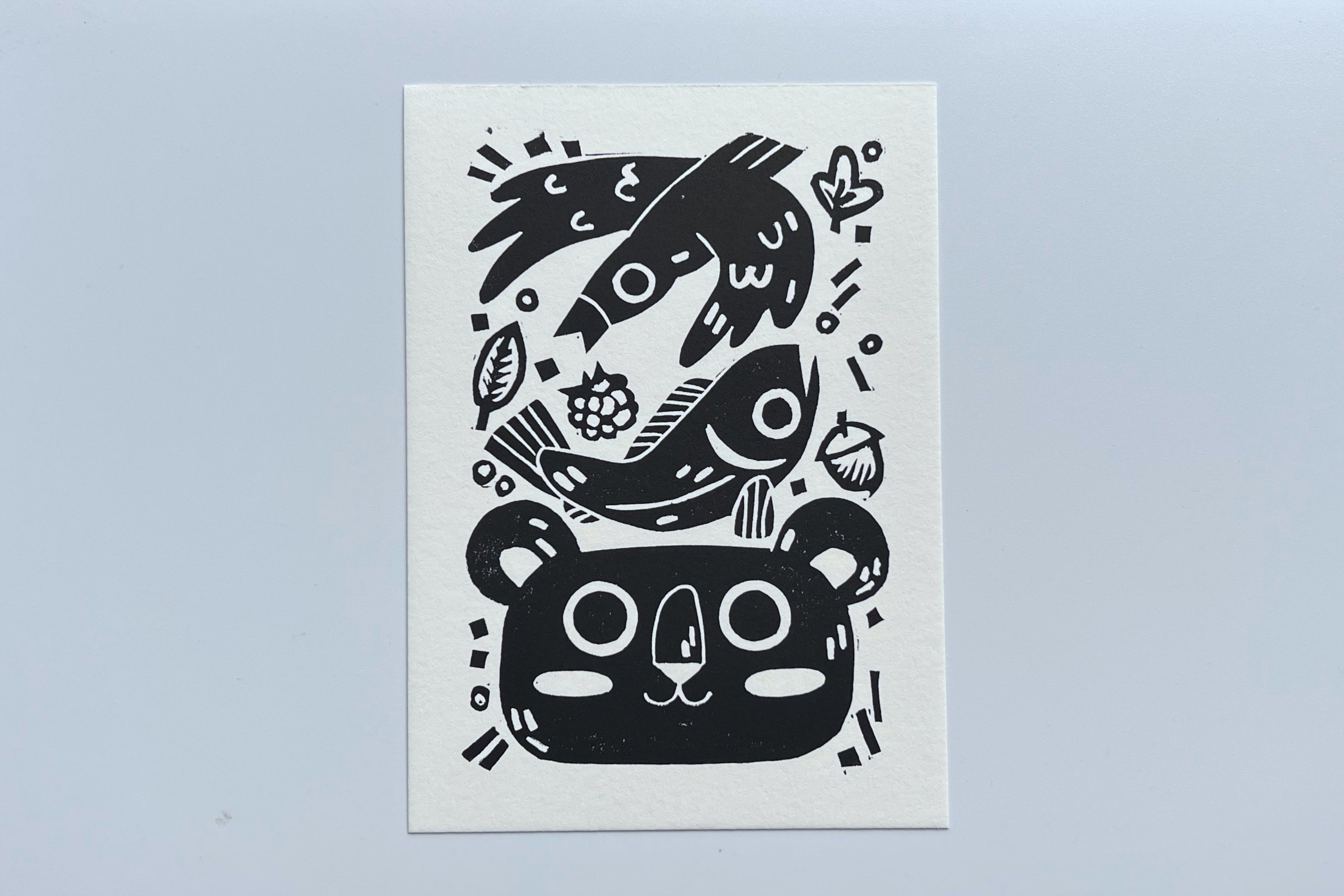 Black ink block print of a bird, fish, leaves, berry, acorn, and bear.