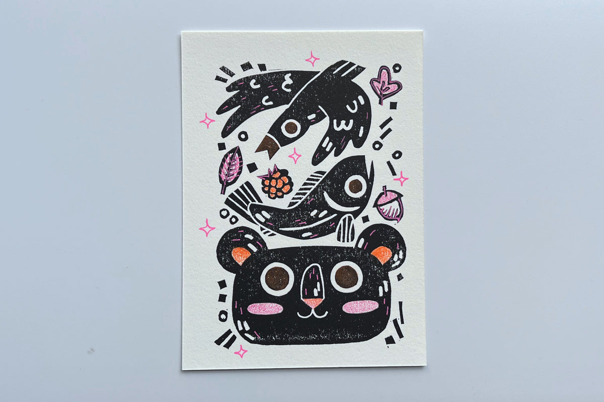 Black ink block print of a bird, fish, leaves, berry, acorn, and bear with colored pencil and POSCA pen coloring.