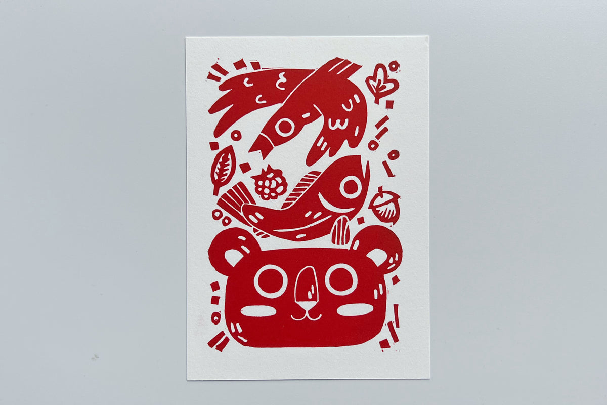 Red ink block print of a bird, fish, leaves, berry, acorn, and bear.