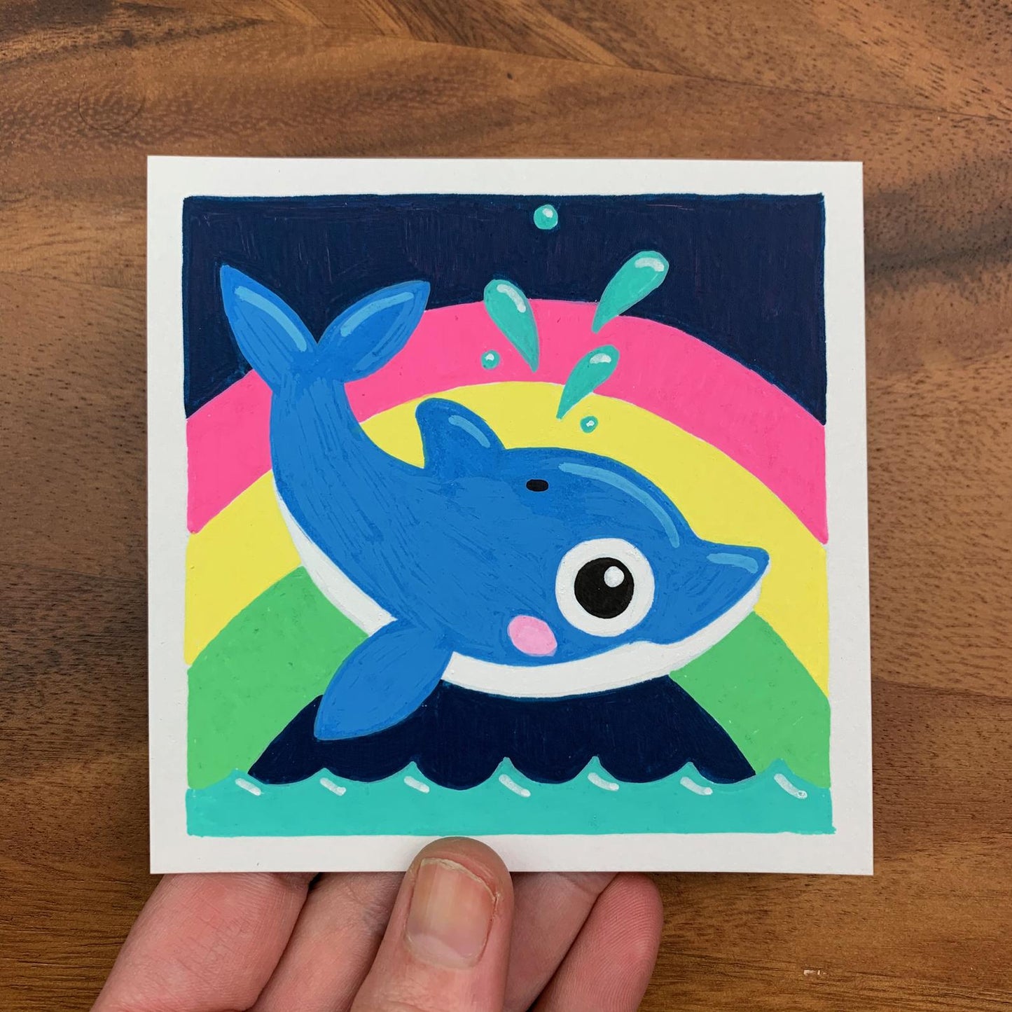 Original artwork of a cute dolphin jumping out of the water and spouting water out of their blow hole with a rainbow behind them. Materials used: Uni-Posca paint markers.