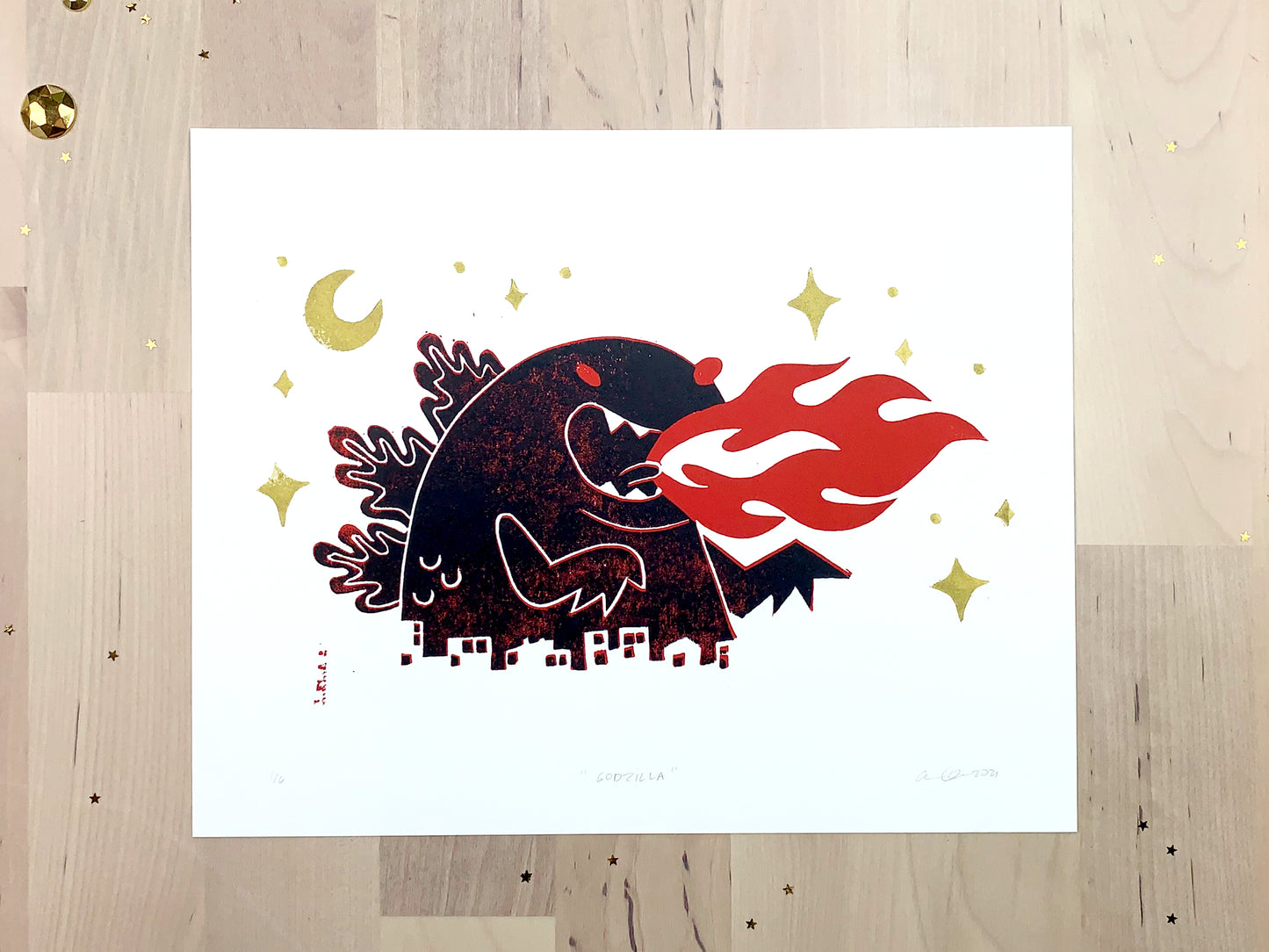 Original limited edition #1 art print by Amber Orenstein. Two color, red and black, reduction block print of a Japanese kaiju monster roaring with flames while destroying a city with gold stars and moon.