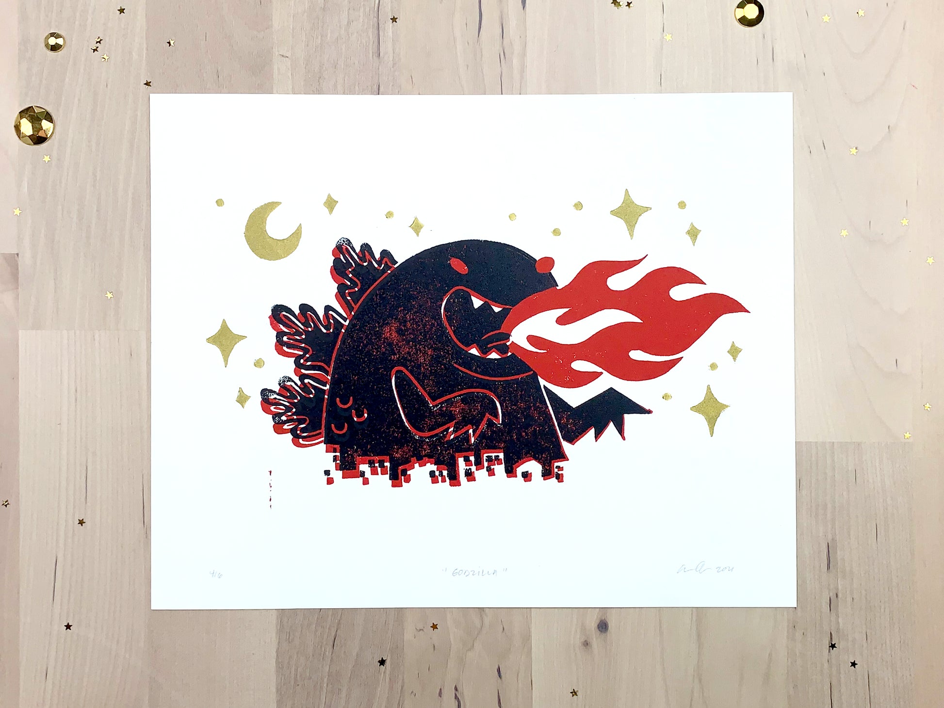 Original limited edition #4 art print by Amber Orenstein. Two color, red and black, reduction block print of a Japanese kaiju monster roaring with flames while destroying a city with gold stars and moon.