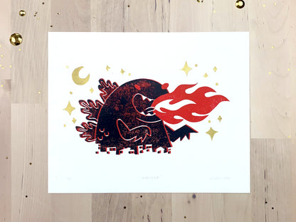 Original limited edition #6 art print by Amber Orenstein. Two color, red and black, reduction block print of a Japanese kaiju monster roaring with flames while destroying a city with gold stars and moon.
