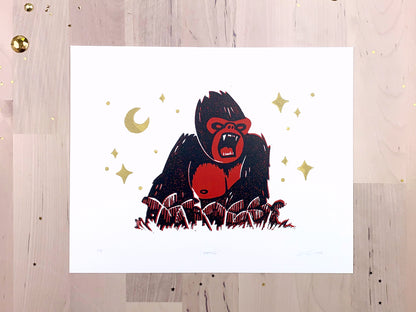 Original limited edition #2 art print by Amber Orenstein. Two color, red and black, reduction block print of a King Kong roaring on his jungle island home with gold stars and moon.
