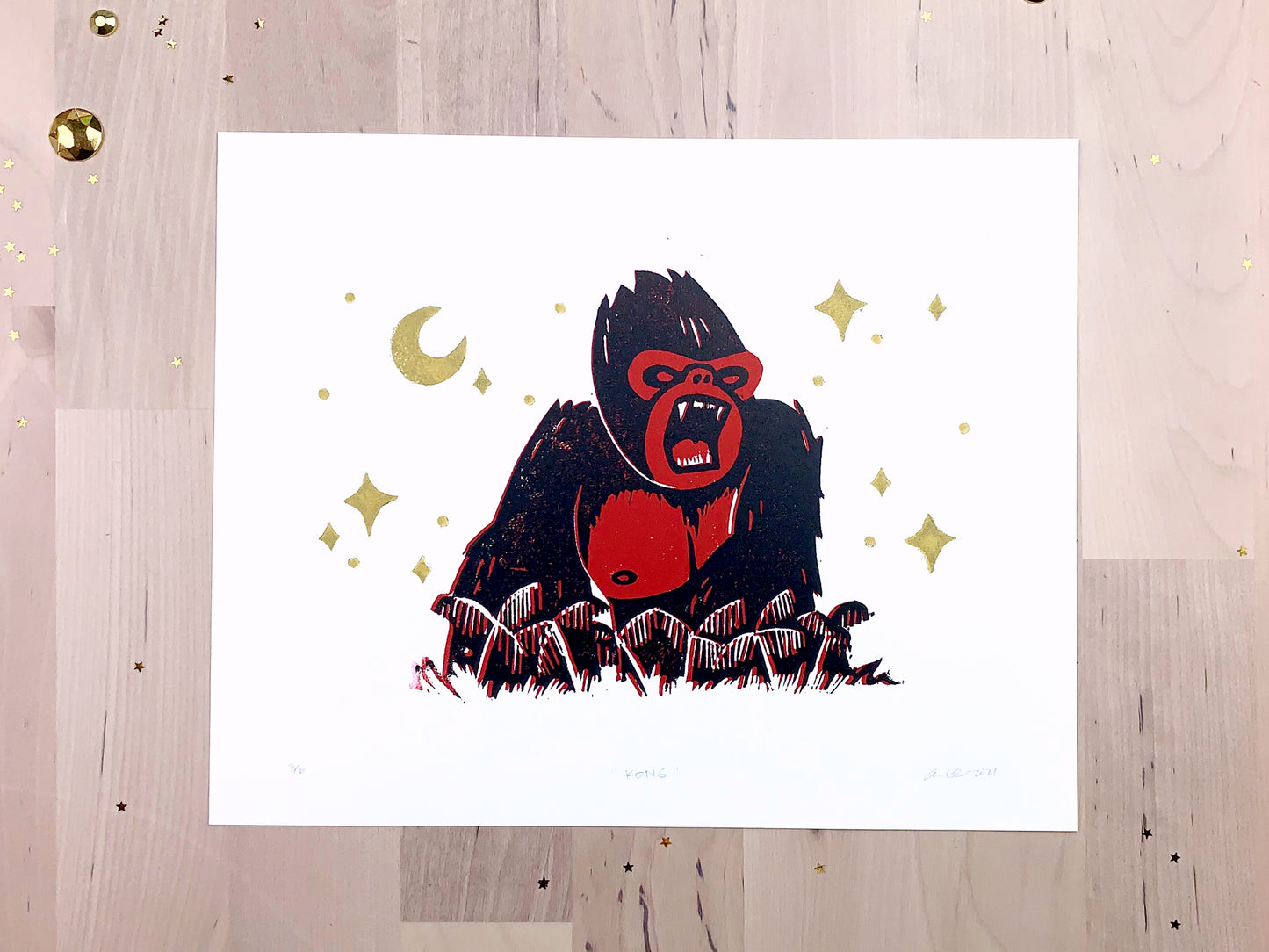 Original limited edition #3 art print by Amber Orenstein. Two color, red and black, reduction block print of a King Kong roaring on his jungle island home with gold stars and moon.