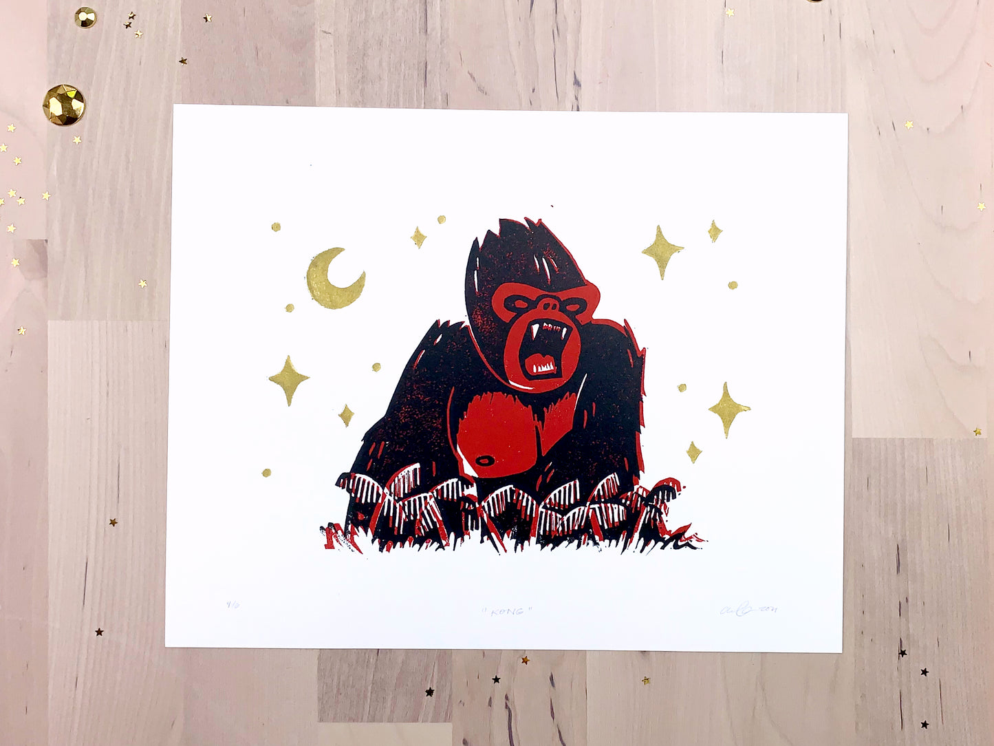 Original limited edition #4 art print by Amber Orenstein. Two color, red and black, reduction block print of a King Kong roaring on his jungle island home with gold stars and moon.