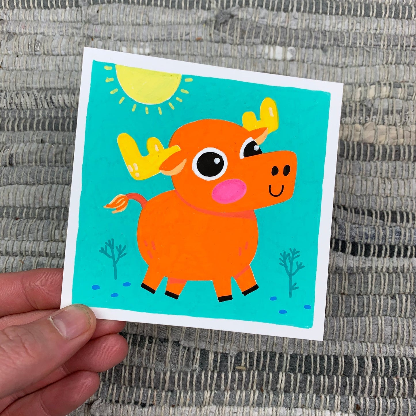 Original artwork of a cute orange moose on a bright teal background with a yellow sun shinning from above. Materials used: Uni-Posca paint markers.