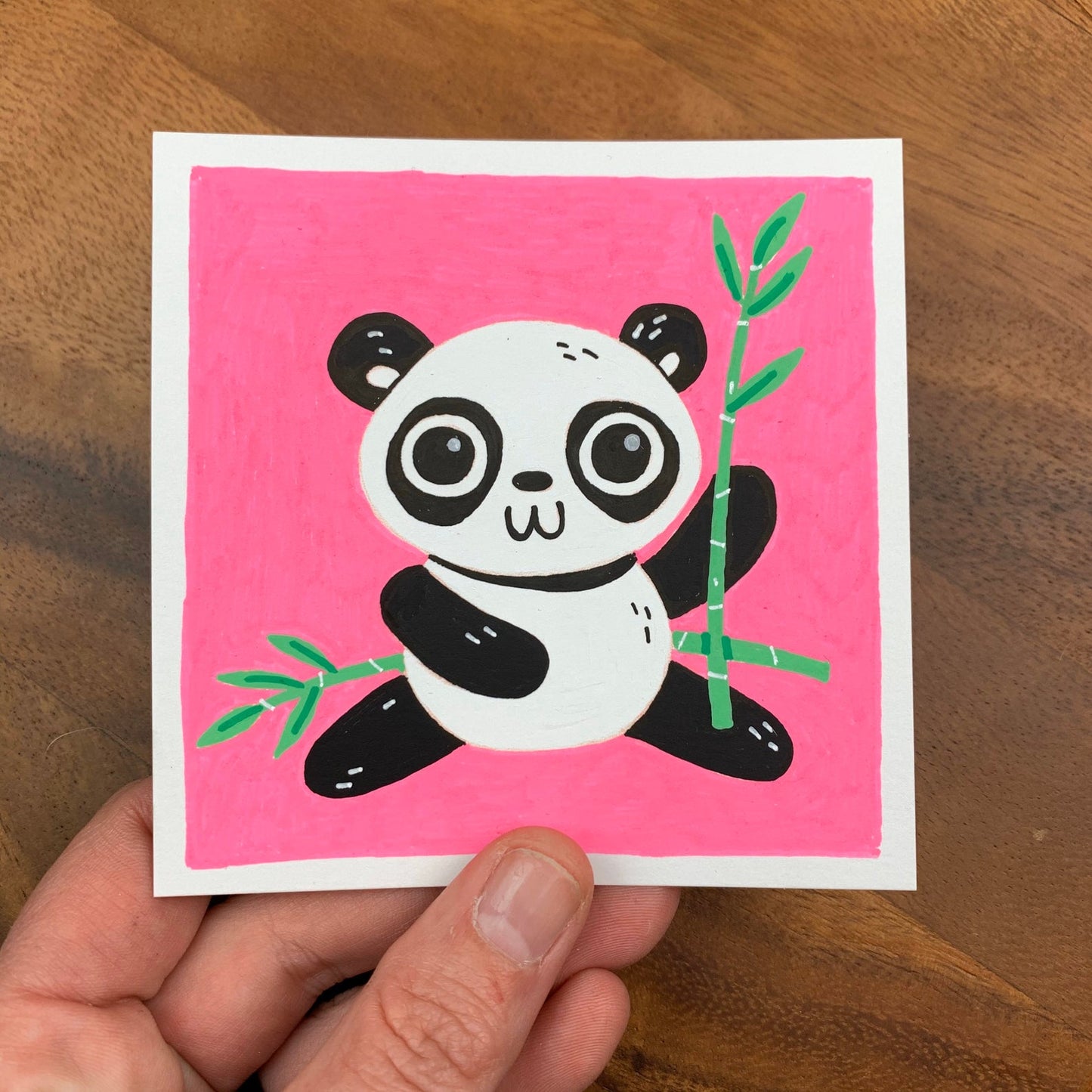 Original artwork of a cute panda bear holding a bamboo on a bright pink background. Materials used: Uni-Posca paint markers.
