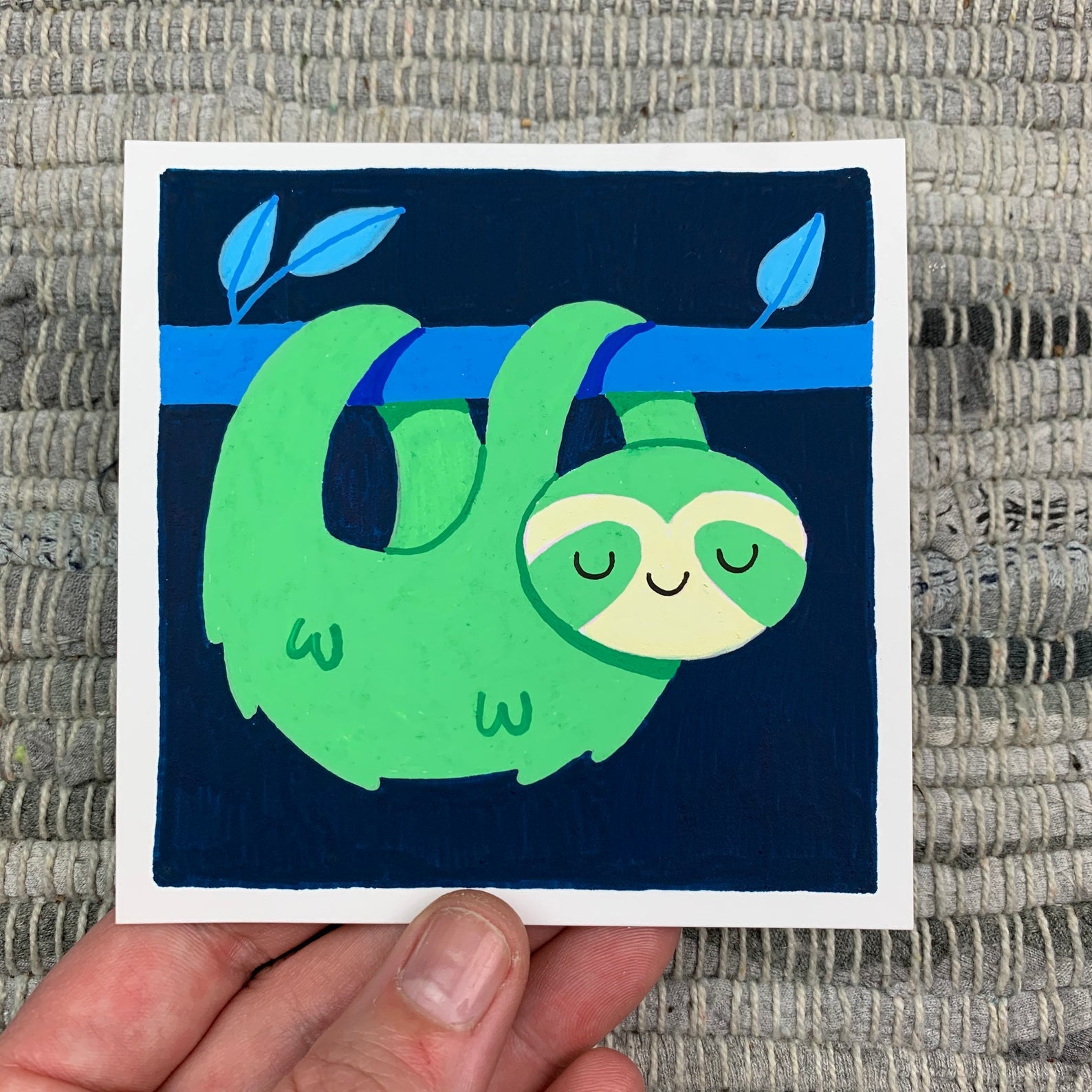 Original artwork of a cute green sloth smiling as he hangs from a blue branch. Materials used: Uni-Posca paint markers.