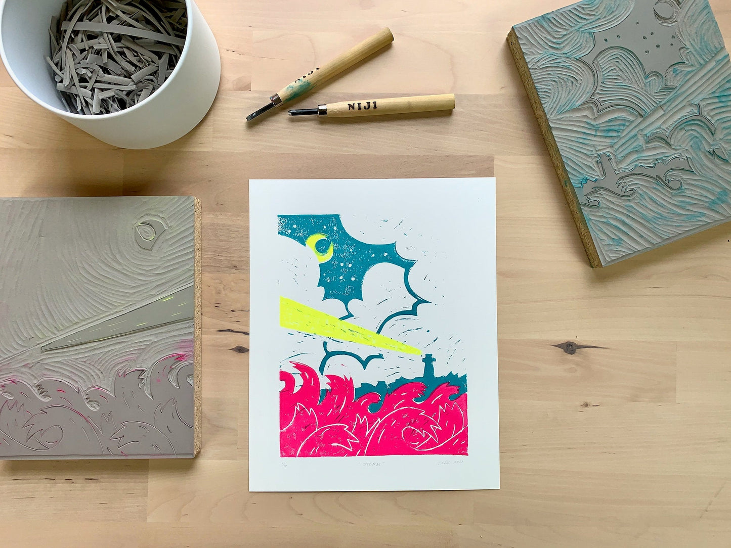 Original linoleum block print artwork showing a lighthouse beam of light in a coastal storm as bright pink waves crash in the foreground.