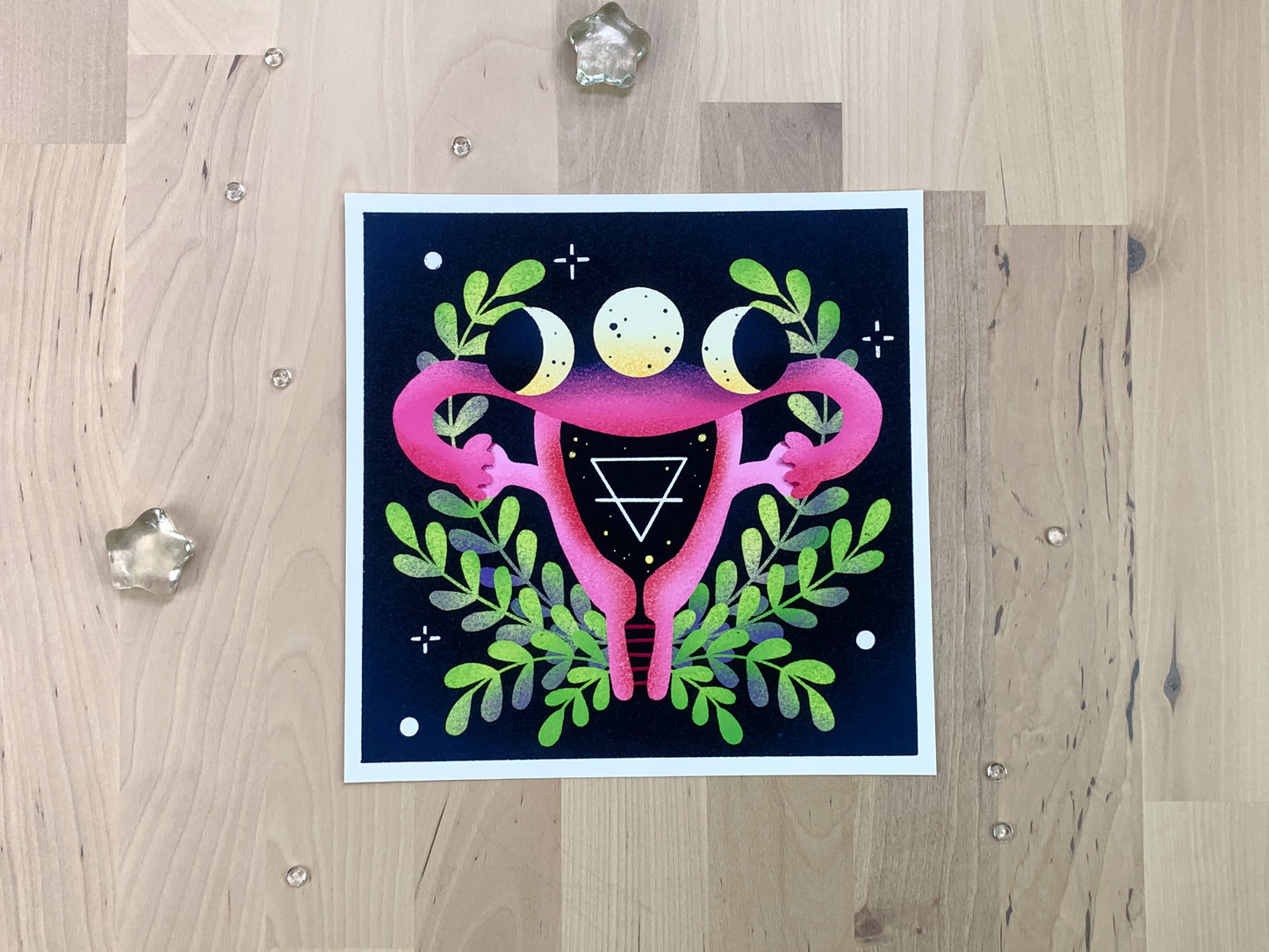 An illustration of a uterus with some witchy moon symbols in front of a wreath.